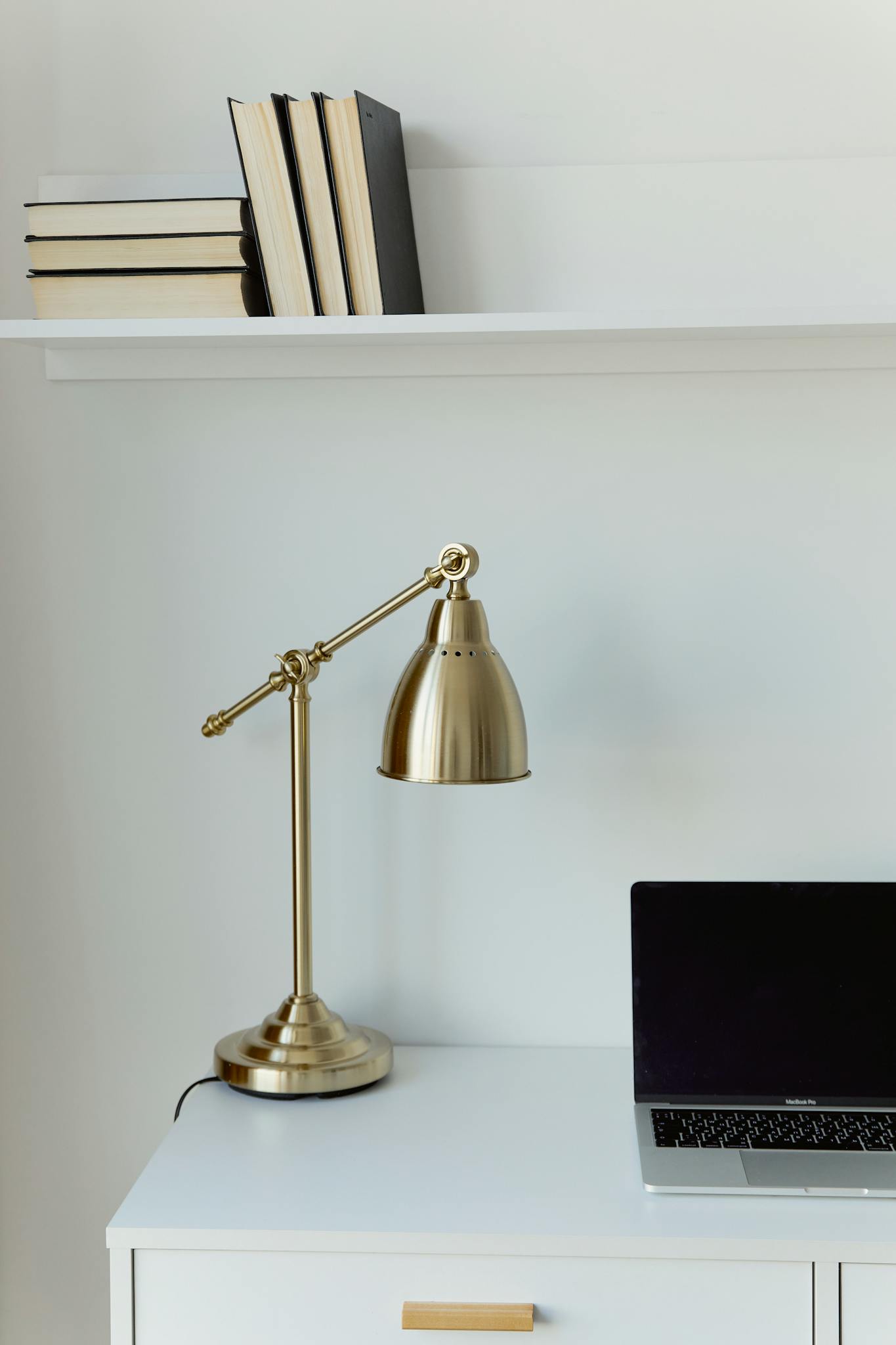 Stylish modern workspace with gold lamp, books, and laptop on a white desk. Perfect for minimalist interiors.